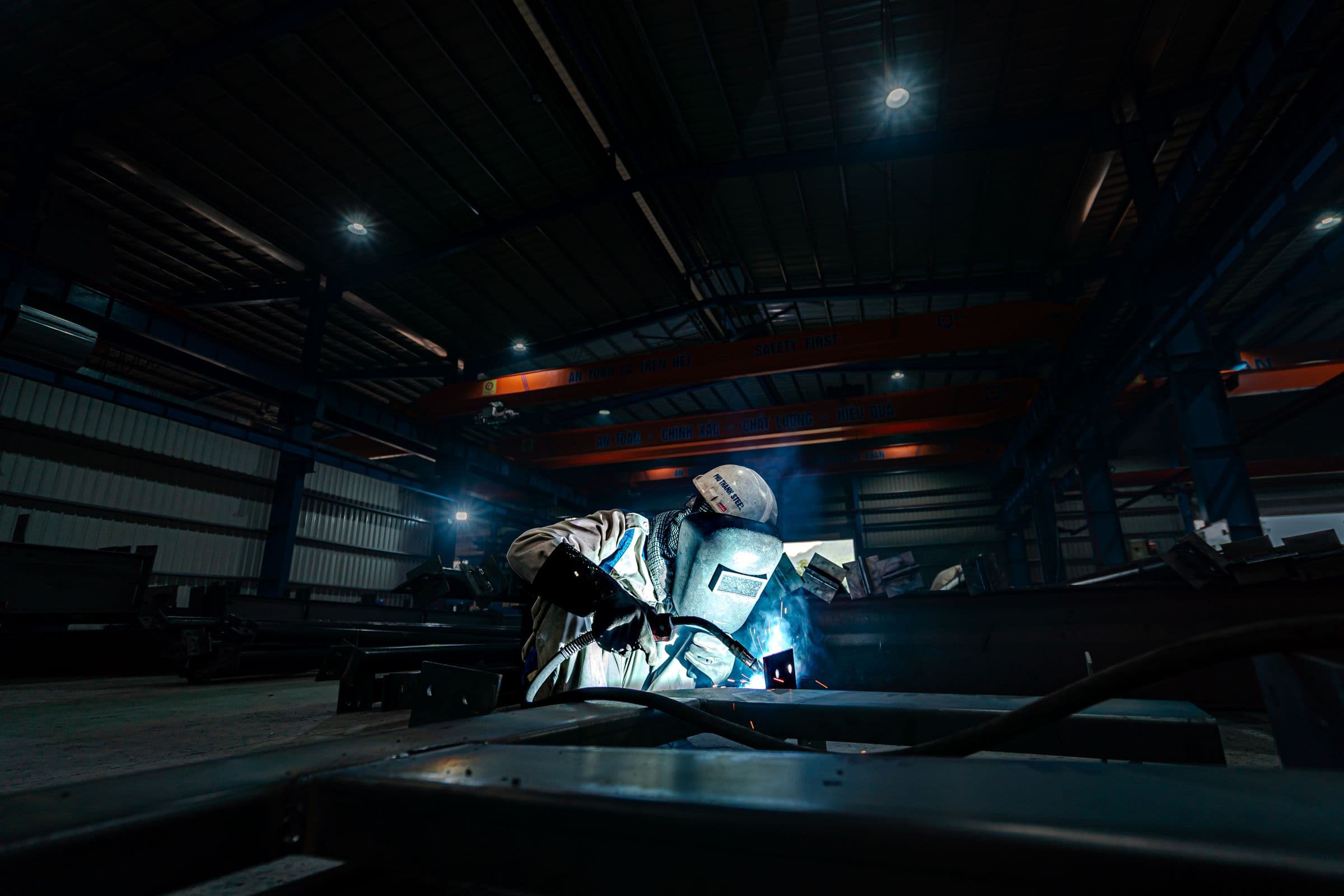 Welder fabricating a steel assembly inside a large industrial shop